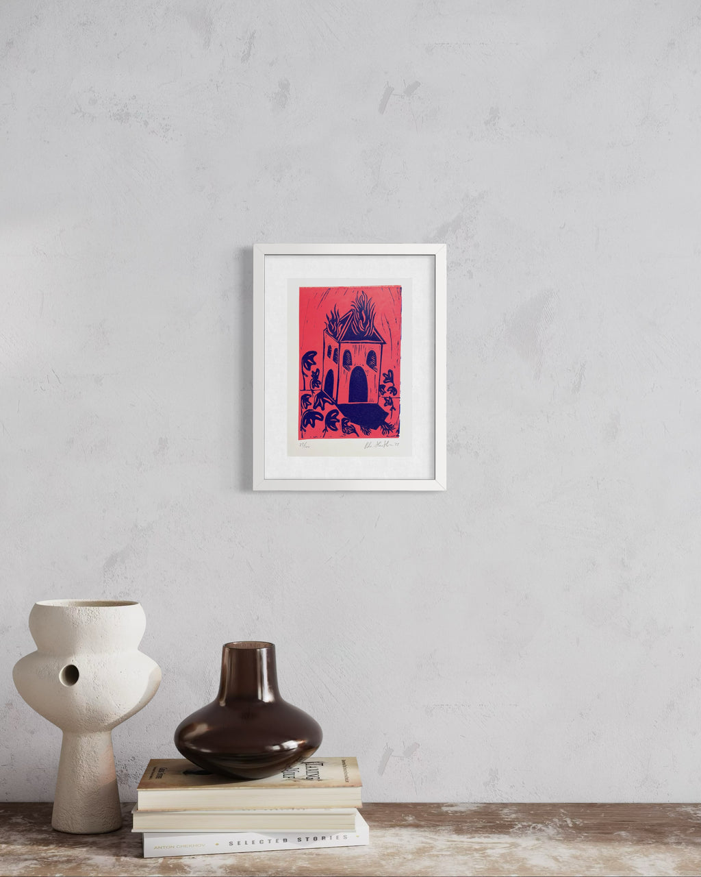 Framed artwork on a wall with two vases and books below