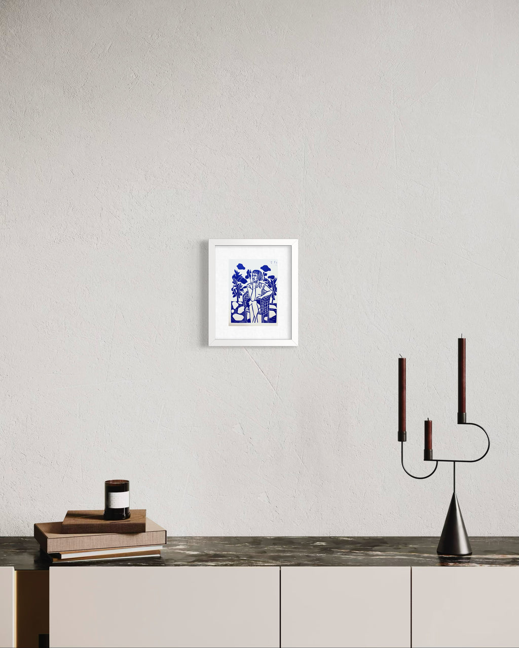 Framed artwork on a wall above a wooden surface with a modern candle holder.