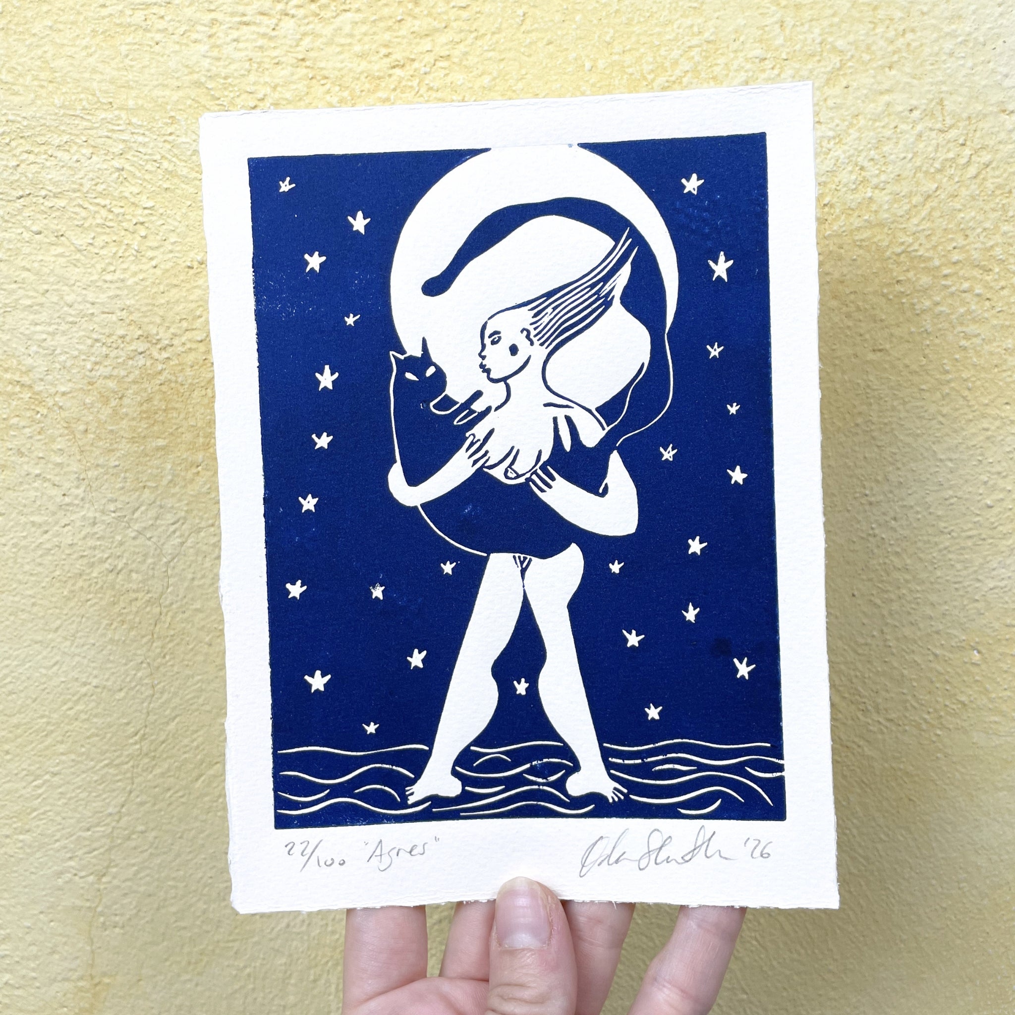 Blue figurative linocut "Agnes", a woman holding a cat with the moon behind them