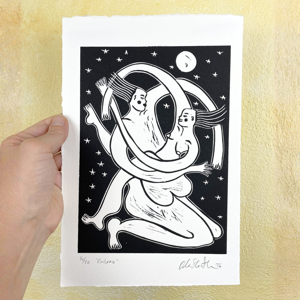 Hand holding a black and white illustration of two people embracing under a moonlit sky.