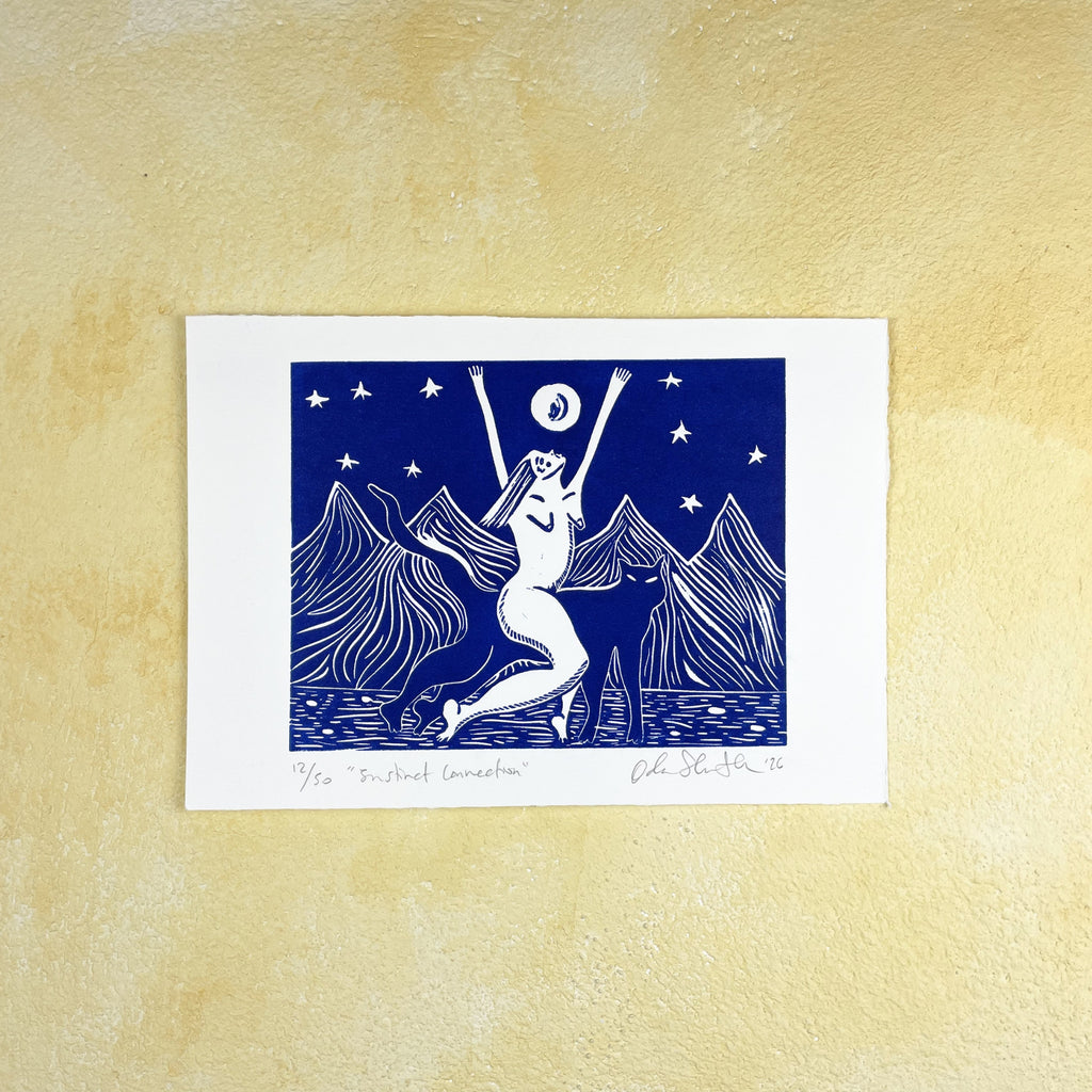 Blue linocut print "Instinct Connection" of a stylized illustration of a woman riding a panther with arms raised against a mountain and starry sky background, on a beige textured surface. 