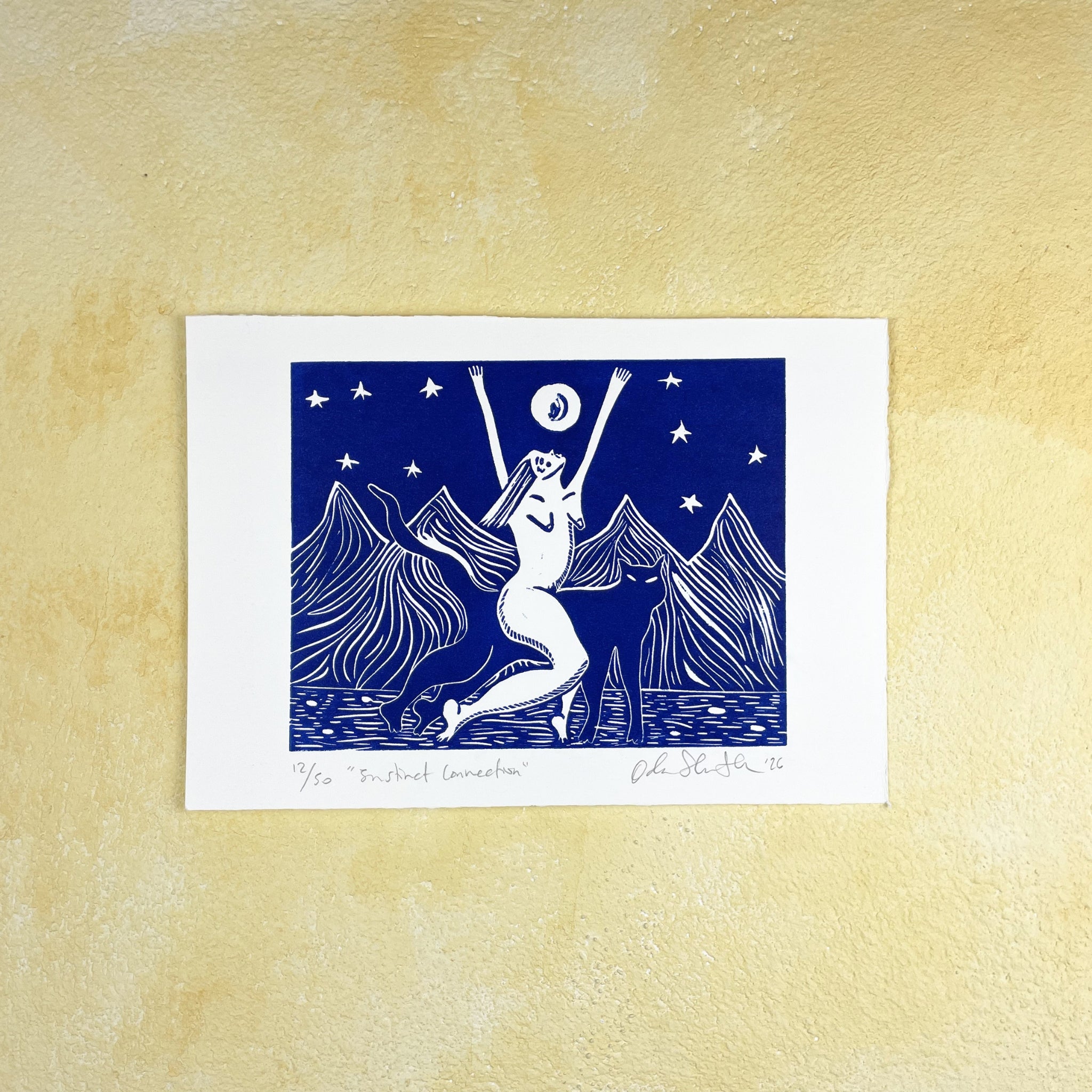 Blue linocut print "Instinct Connection" of a stylized illustration of a woman riding a panther with arms raised against a mountain and starry sky background, on a beige textured surface. 