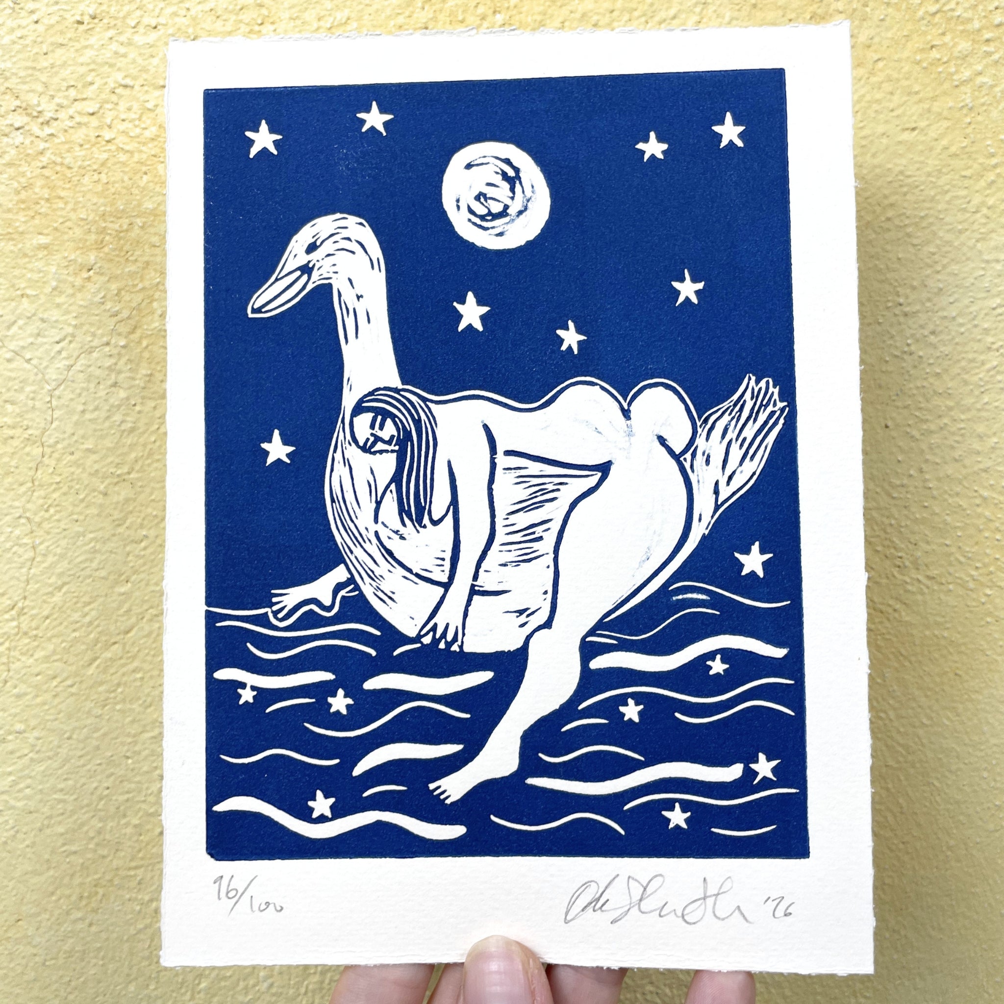White duck illustration on a blue background with stars and moon, held against a gold textured background.