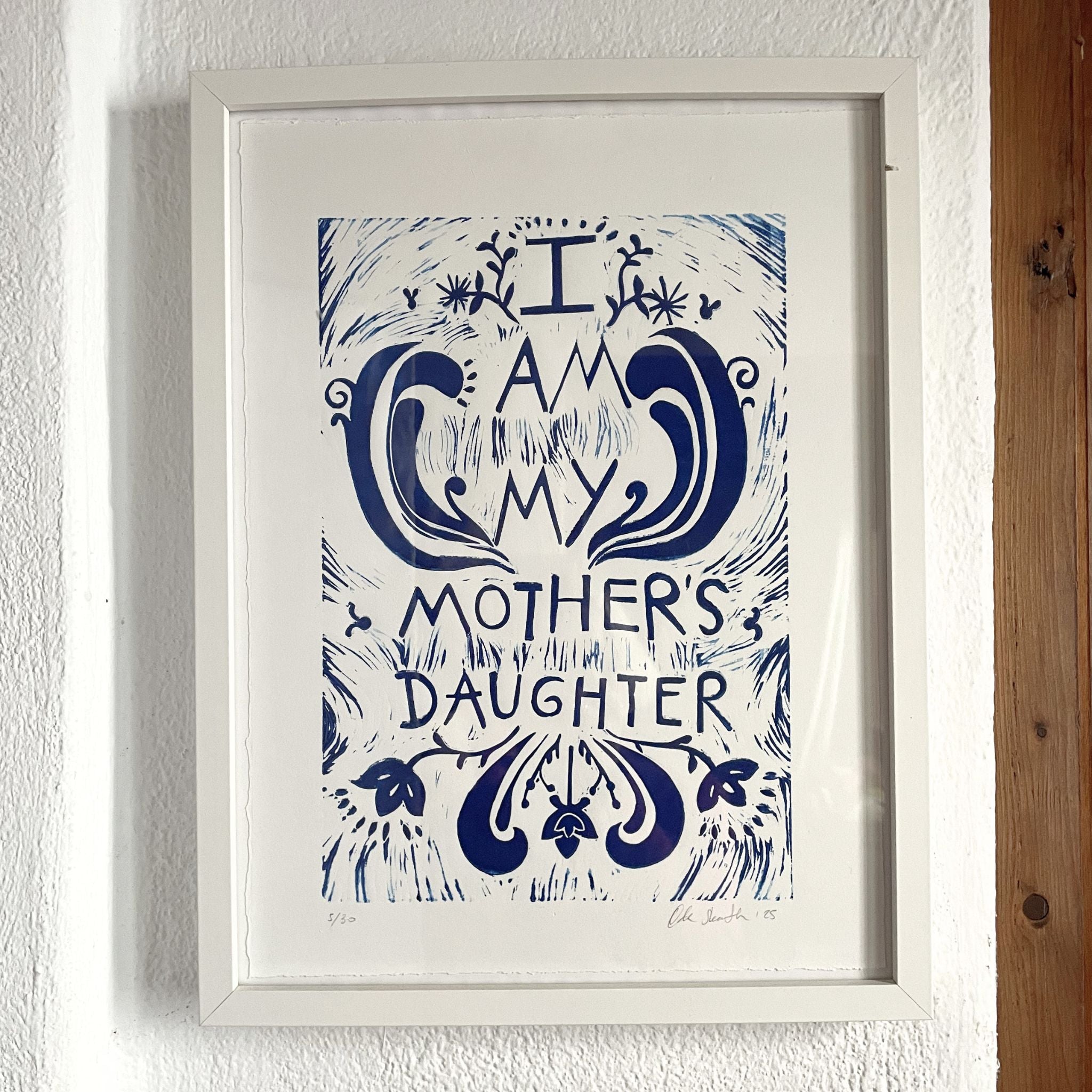 Framed artwork with 'I am my mother's daughter' text on a white wall.